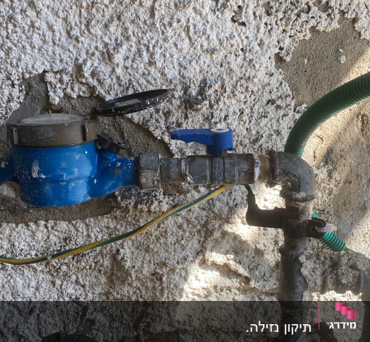 מד מים כחול עם צינורות וברזים על קיר
